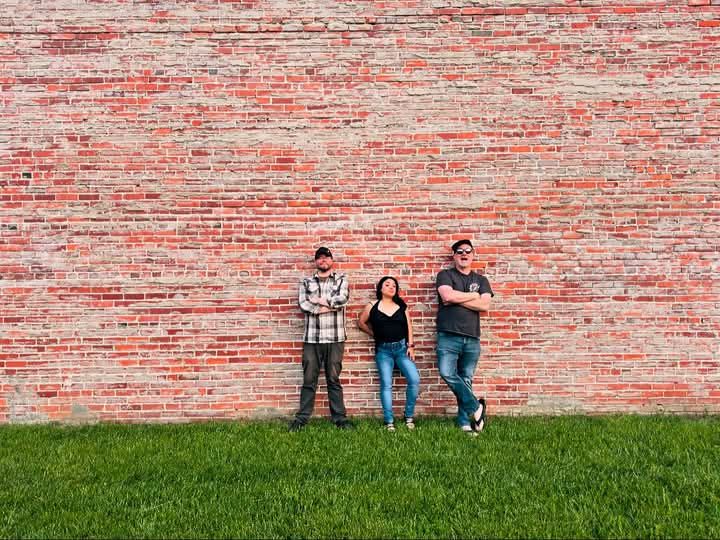 picture of band 'New Groove' in front of a brick wall, standing on grass